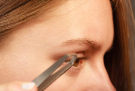 Woman tweezing eyebrows depilating with tweezers